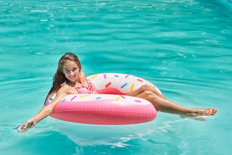 Smiling girl have fun floating on inflatable donut in blue swimming pool