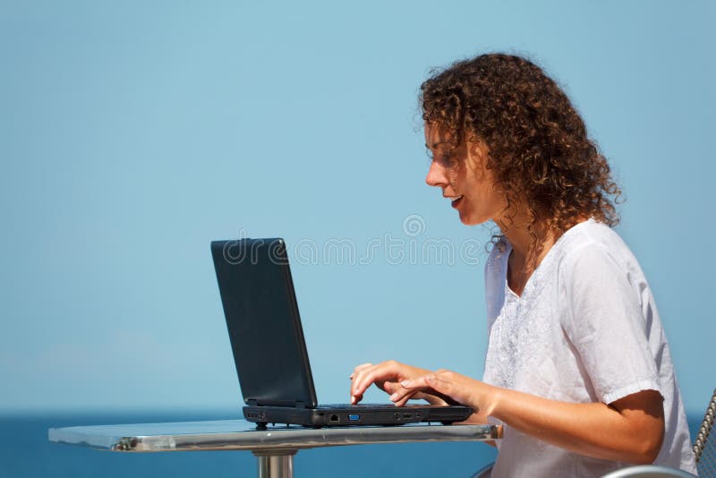 Smiling girl with laptop. Sits at table on beach royalty free stock photos Smiling girl with laptop. Sits at table on beach royalty free stock photos