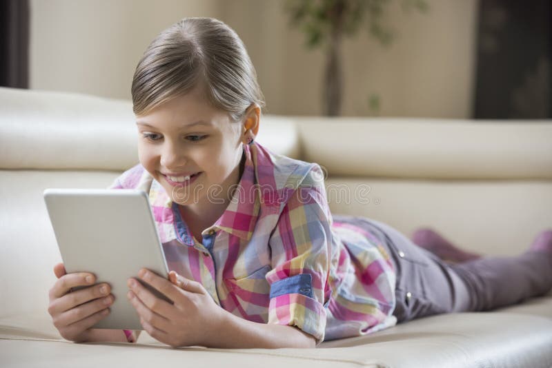 Smiling girl using tablet PC while lying on sofa at home