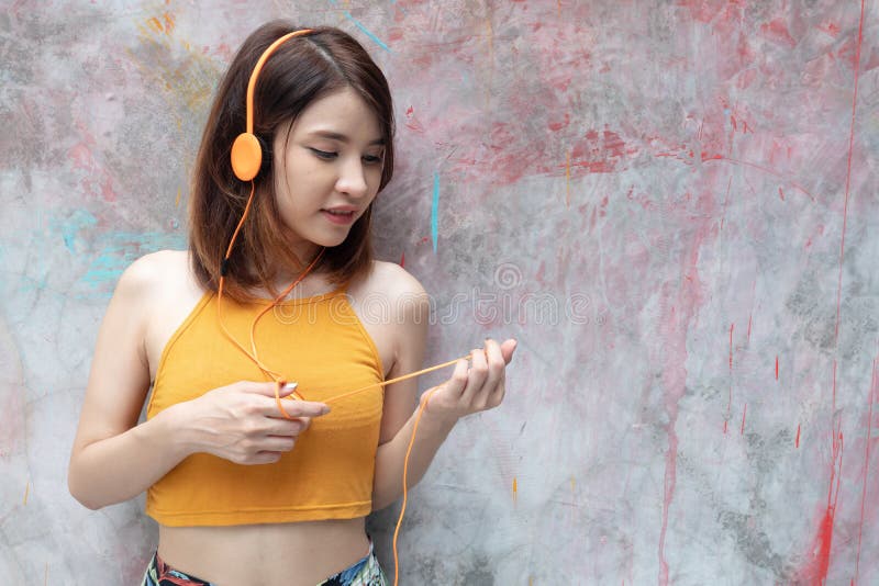 Smiling girl in yellow summer clothes listening music with earphones and mobile phone on light background with copy space..Young