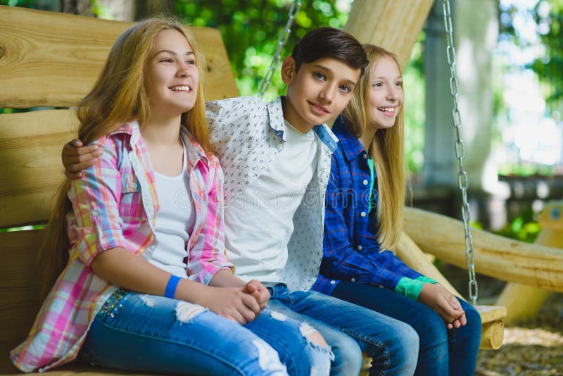 Smiling girls and boy having fun at playground. Children playing outdoors in summer. Teenagers on a swing.