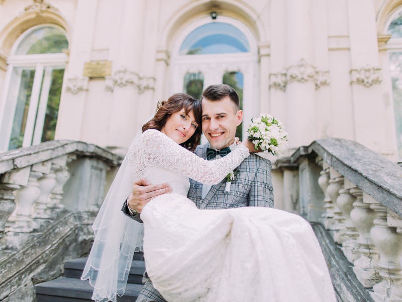 The smiling groom is carrying the cheerful bride. The horizontal view.