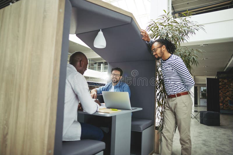 Diverse team of creative professionals working on a project together while sitting in a meeting pod in the lobby of a modern office. Diverse team of creative professionals working on a project together while sitting in a meeting pod in the lobby of a modern office