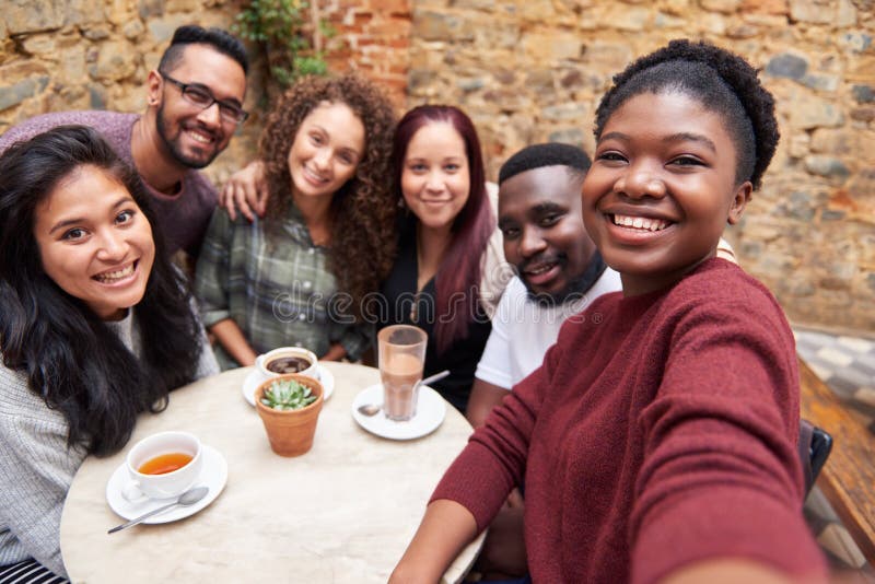 Diverse young friends taking selfies together in a cafe courtyard stock images