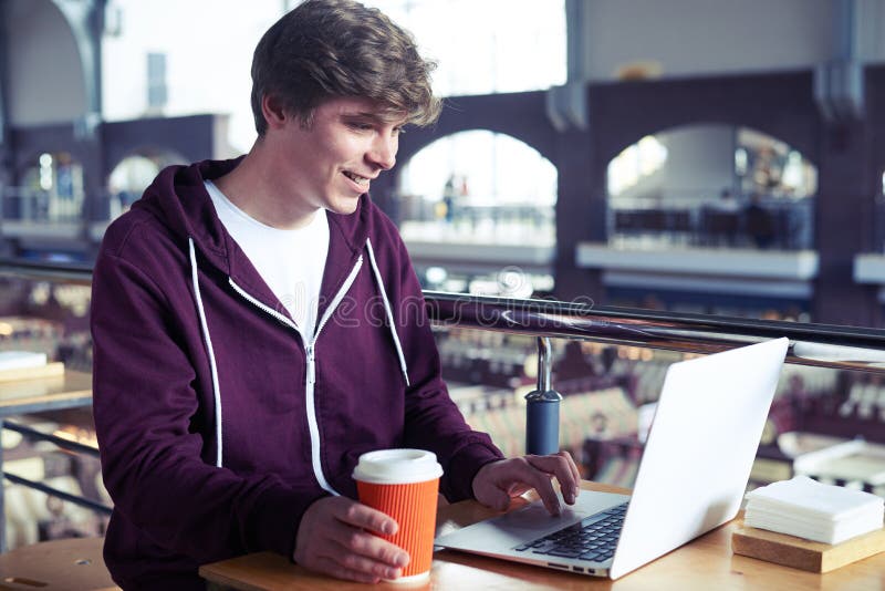 Smiling guy printing in laptop over paper cup of coffee