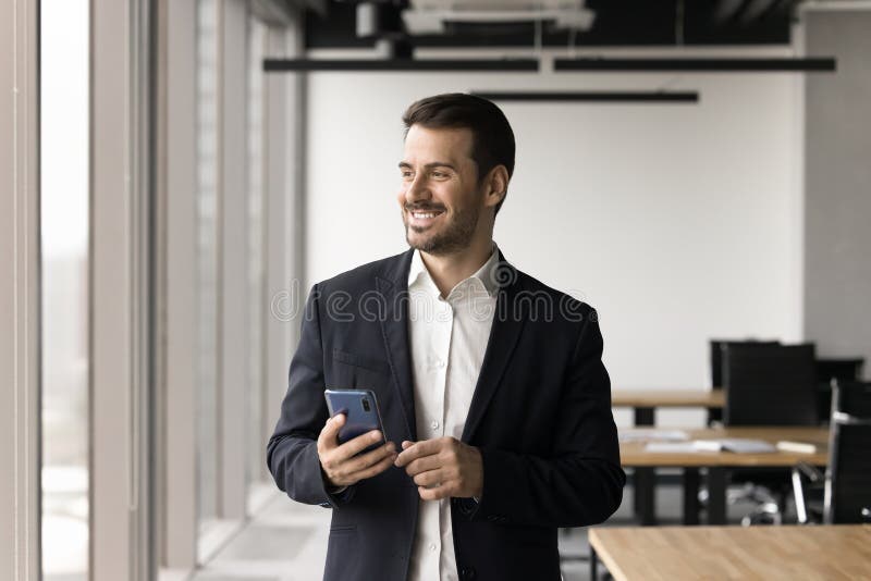 Smiling handsome businessman dressed in suit holding smart phone stock photo
