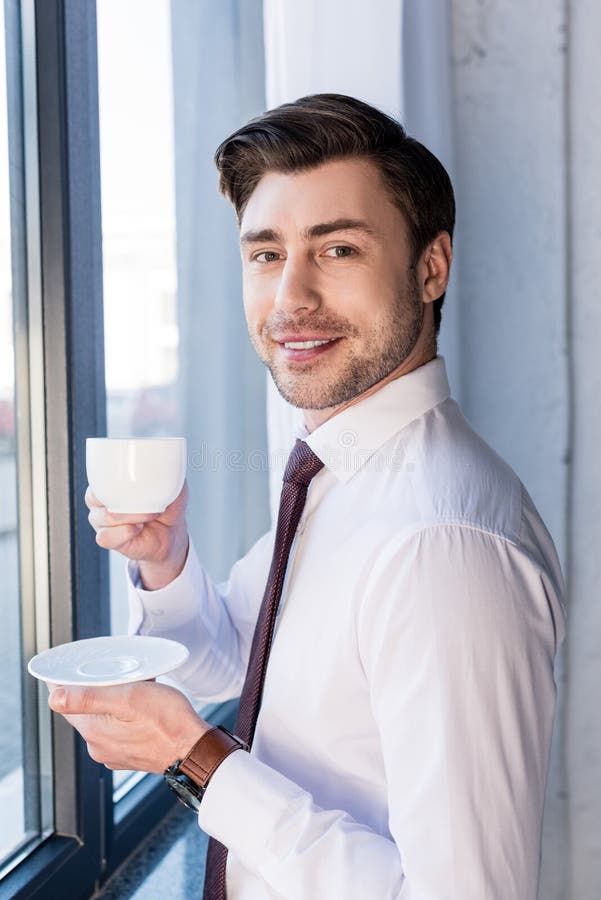 Smiling Handsome Man Standing by Window, Holding Coffee Up and Looking ...