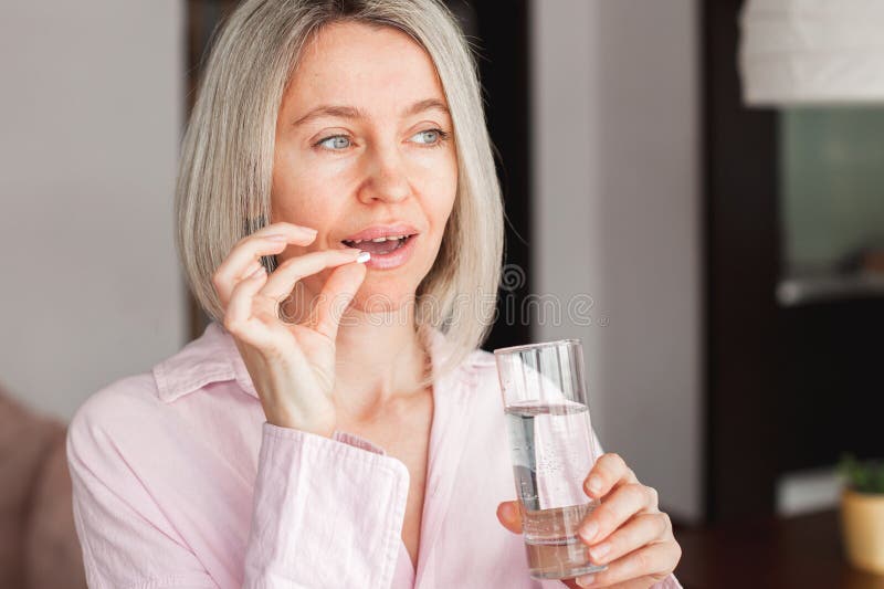 Middle aged woman holding pill and glass of fresh water