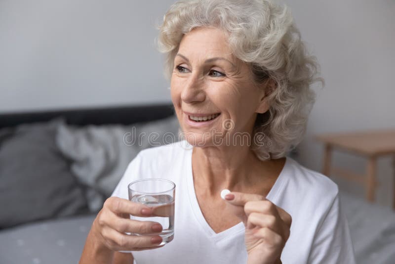 Smiling senior woman holding glass of water taking daily pill