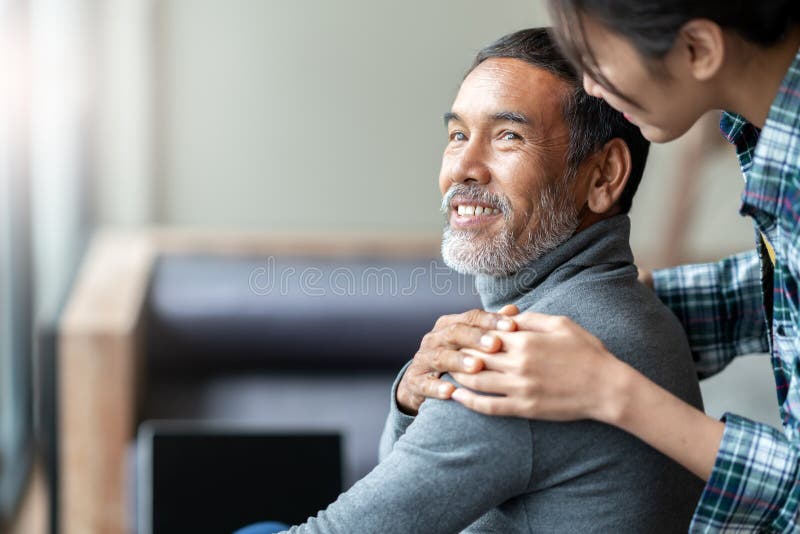 Smiling happy older asian father with stylish short beard touching daughter`s hand on shoulder looking