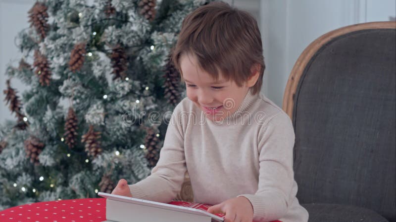 Smiling kid boy sitting on a chair and playing with tablet during Christmas time royalty free stock image Smiling kid boy sitting on a chair and playing with tablet during Christmas time royalty free stock image