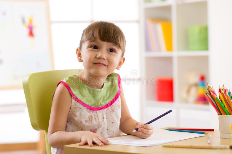 Smiling kid drawing with color pencils in day care center