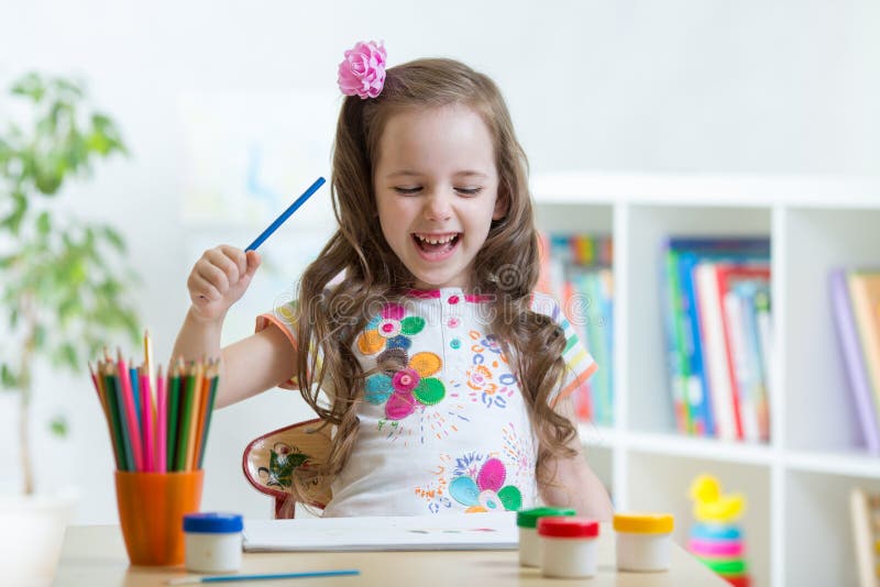 Smiling kid drawing with color pencils in day care center