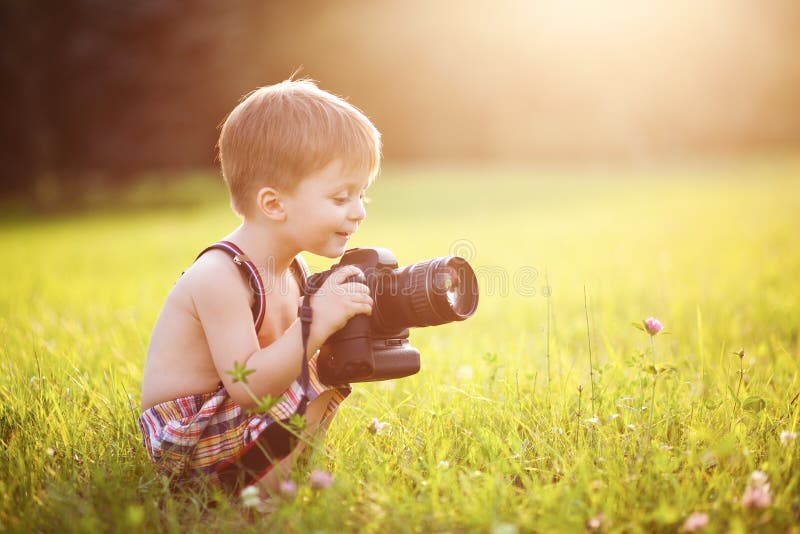 Krásne usmievavé dieťa, chlapec drží DSLR fotoaparát v parku.