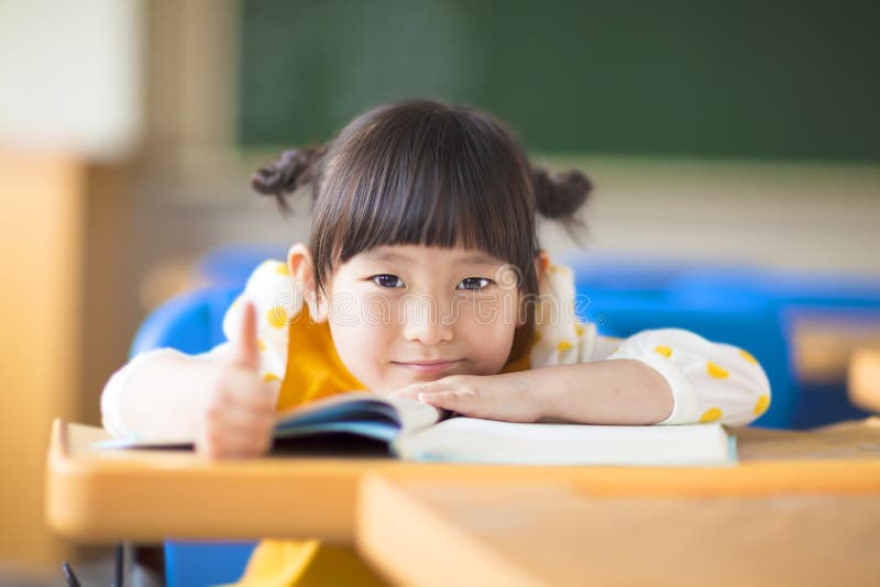 Smiling kid lie prone on a desk and thumb up