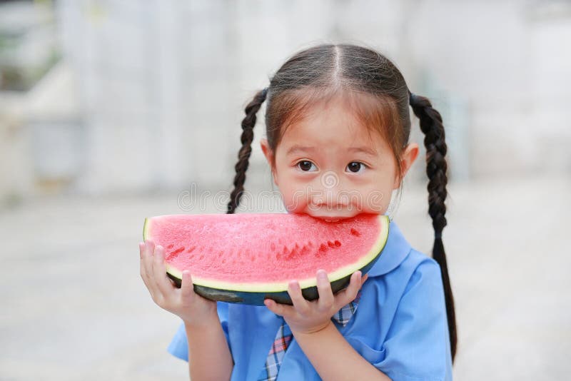 Smiling little Asian child girl in school uniform enjoy eating watermelon outdoors stock photography Smiling little Asian child girl in school uniform enjoy eating watermelon outdoors stock photography
