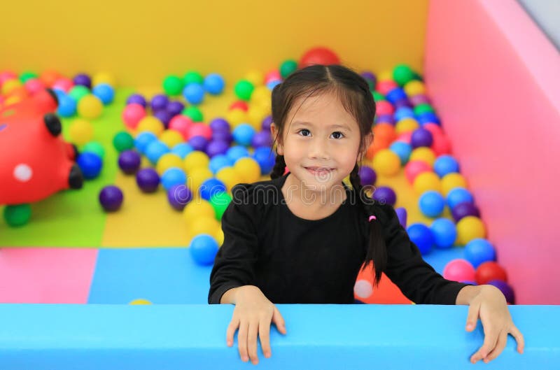 Smiling little Asian girl playing in a kids` ball pit at a playground