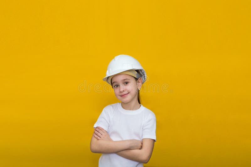 Smiling little girl in a construction white helmet crossed her arms over her chest on a yellow background stock image Smiling little girl in a construction white helmet crossed her arms over her chest on a yellow background stock image