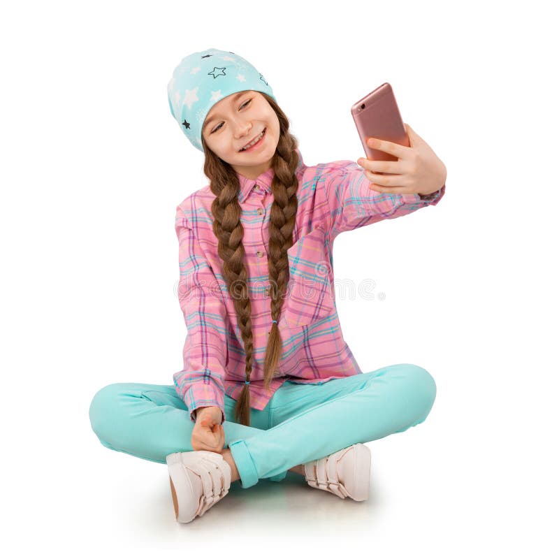 Smiling little girl holding mobile phone and making selfie on white background