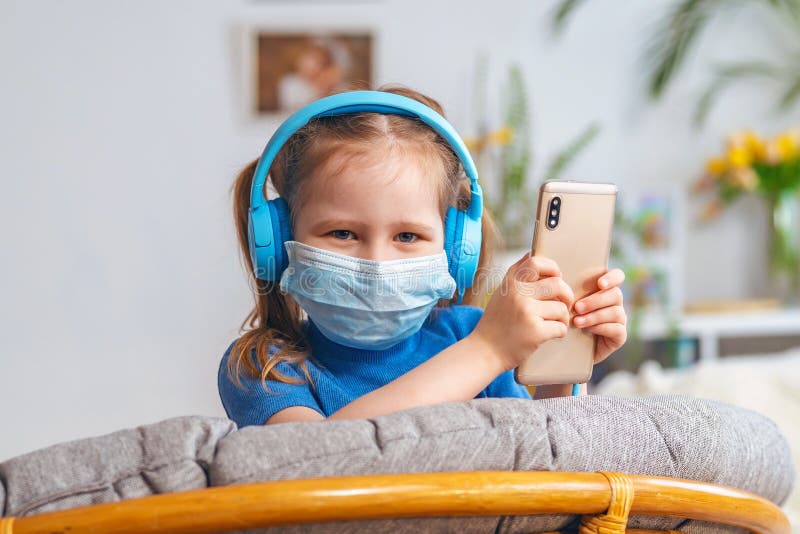 Smiling little girl a kid in a mask and blue headphones holding a mobile phone royalty free stock photo Smiling little girl a kid in a mask and blue headphones holding a mobile phone royalty free stock photo