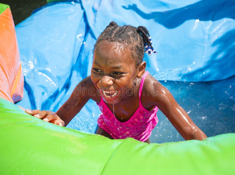 Smiling little girl playing outdoors on an inflatable bounce house water slide stock photography