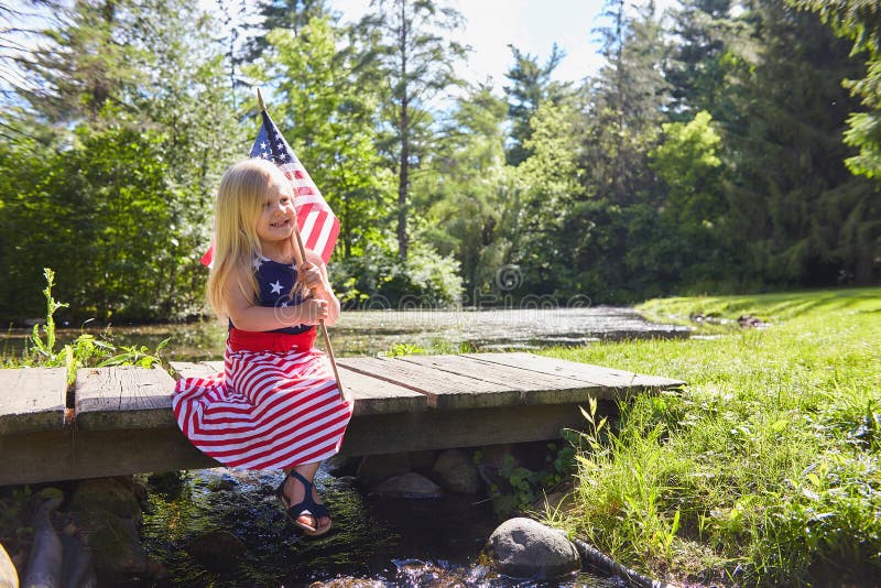 Smiling little girl sitting on bridge with American flag