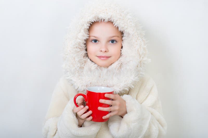 Smiling little girl in winter clothes with a red cup of hot drink.