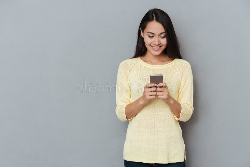 Smiling lovely young woman standing and using cell phone