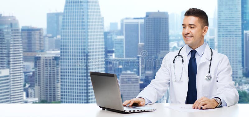 Smiling male doctor with laptop sitting at table