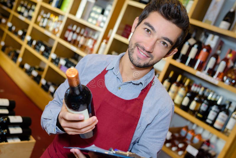 Smiling man seller having bottle wine in shop