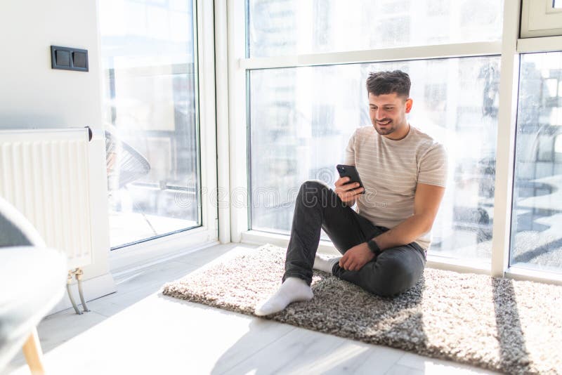 Smiling Young Man Sitting on Floor and Texting Friend Stock Image