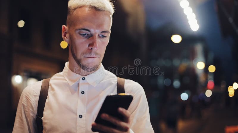 Smiling man usingn smartphone in night city. Handsome young man using smartphone at night and drinking ice coffee stock footage