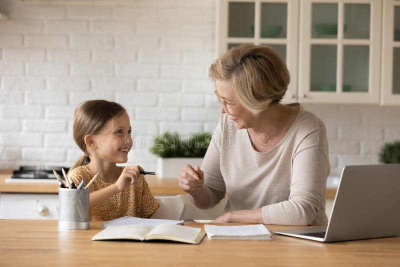 Smiling grandmother help granddaughter with homework assignment. Smiling mature grandmother help small Caucasian girl child with homework assignment at home stock photos Smiling grandmother help granddaughter with homework assignment. Smiling mature grandmother help small Caucasian girl child with homework assignment at home stock photos