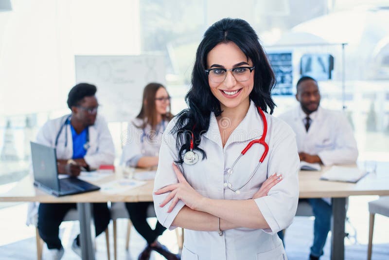 Smiling medical doctor woman with stethoscope standing in front of medic team at hospital. Attractive young female royalty free stock image Smiling medical doctor woman with stethoscope standing in front of medic team at hospital. Attractive young female royalty free stock image
