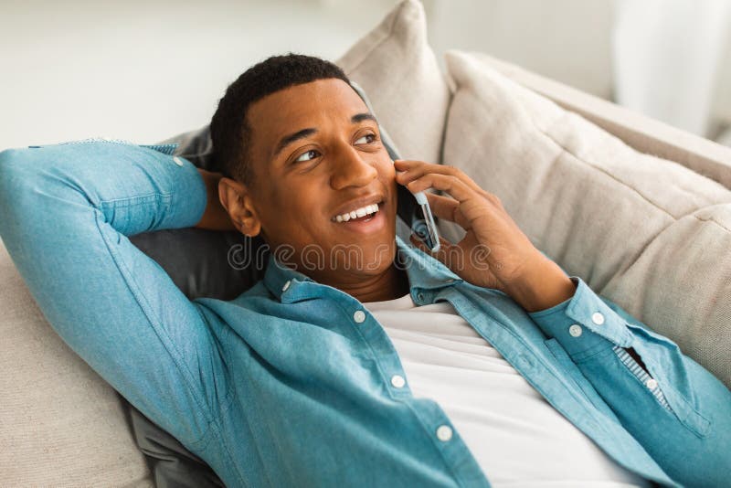 Smiling Millennial African American Man Lying on Sofa Making Phone Call