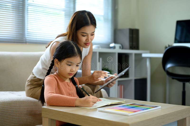 Smiling mom supporting her little girl with schoolwork at home stock image