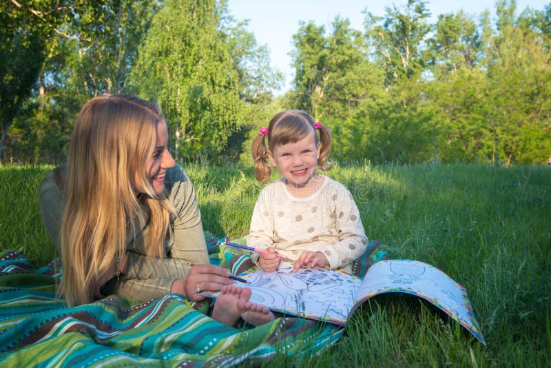 Smiling mother and daughter are painting in a book in the park