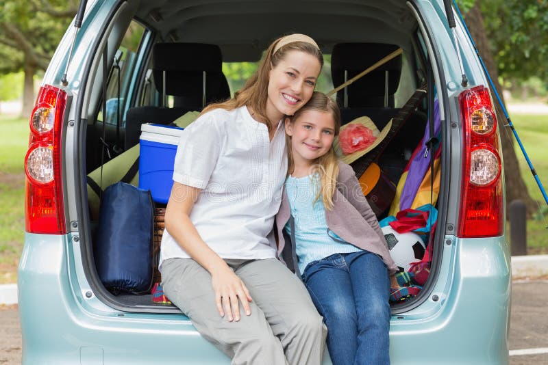 Smiling mother and daughter sitting in car trunk