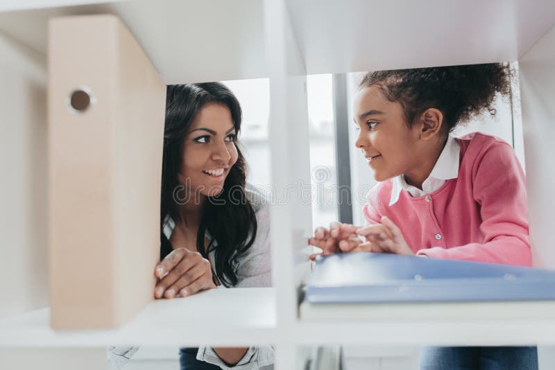 Smiling mother and daughter standing near bookshelves and smiling each other royalty free stock photography Smiling mother and daughter standing near bookshelves and smiling each other royalty free stock photography