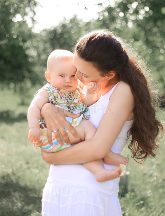 Smiling mother holding her little daughter in arms, talking, looking at baby with love and adoration stock photo Smiling mother holding her little daughter in arms, talking, looking at baby with love and adoration stock photo