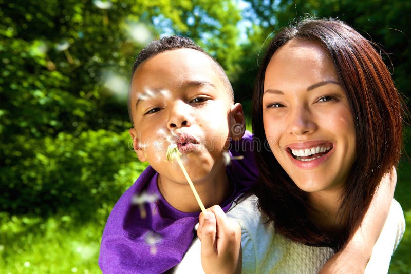 Close up portrait of a smiling mother with son blowing dandelion outdoors