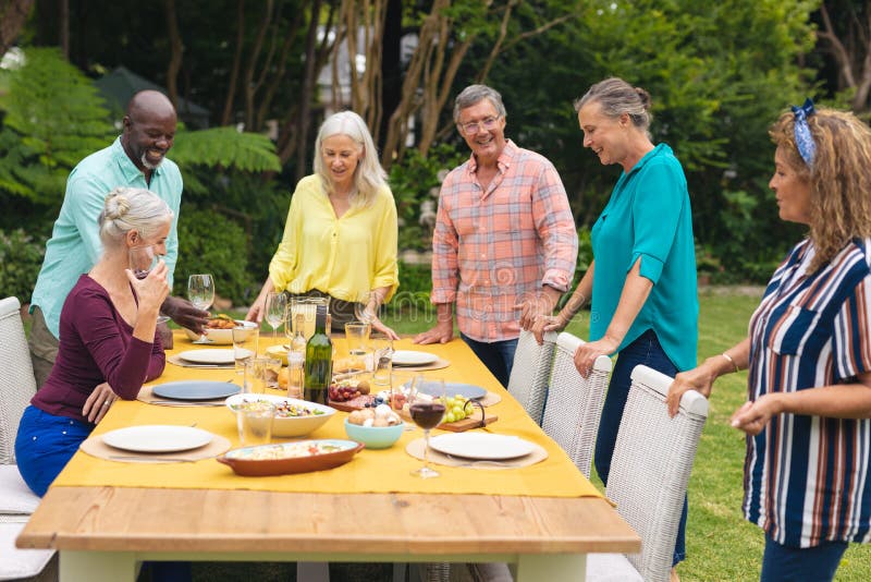 Smiling multiracial senior male and female friends with food at table in backyard