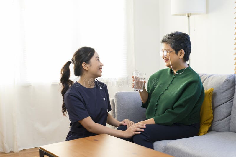 Smiling nurse giving glass of water to senior asian woman in nursing home