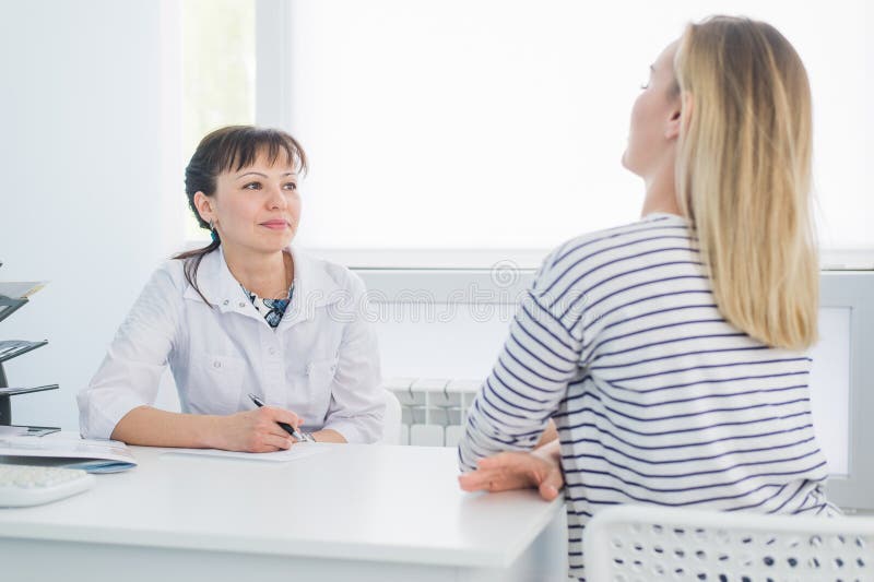 Smiling patient receiving a medical consultation and looking at camera, the female doctor is sitting at desk on the royalty free stock photos Smiling patient receiving a medical consultation and looking at camera, the female doctor is sitting at desk on the royalty free stock photos