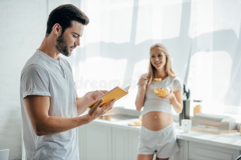 Smiling Pregnant Wife With Fruits Salad And Husband With Book In