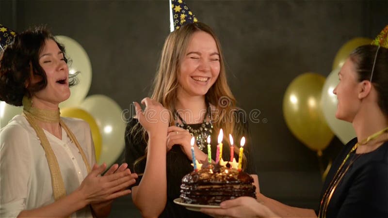 Smiling Pretty Girl Blowing Candles on a Chocolate Cake, Having Fun with Her Two Friends. Women Singing Happy Birthday