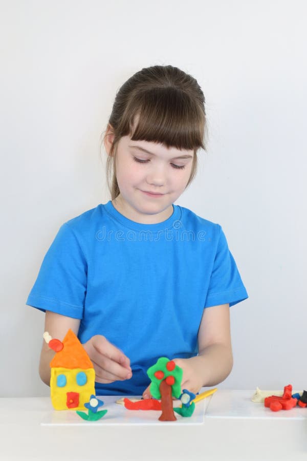 Smiling pretty girl molds toys from plasticine on table stock photo Smiling pretty girl molds toys from plasticine on table stock photo