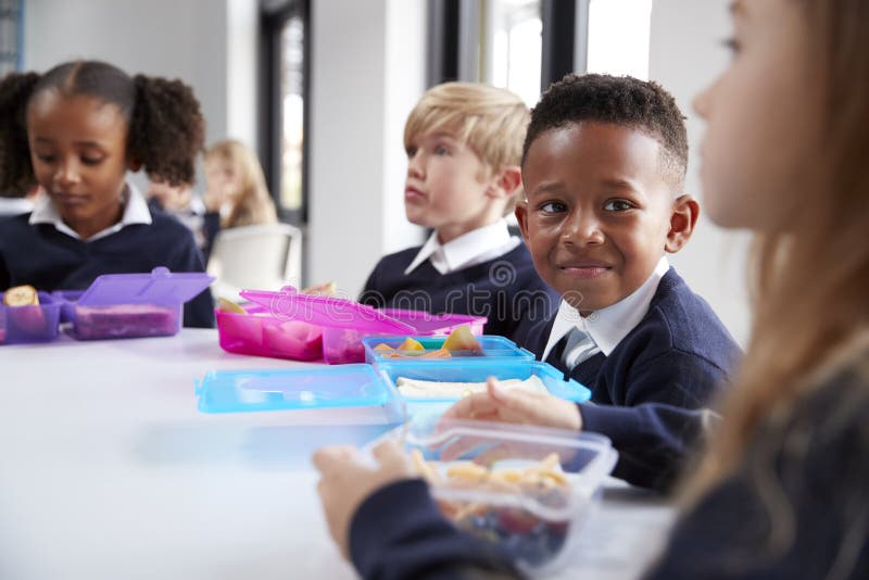 Smiling primary school kids sitting at a table eating their packed lunches together, selective focus stock image Smiling primary school kids sitting at a table eating their packed lunches together, selective focus stock image