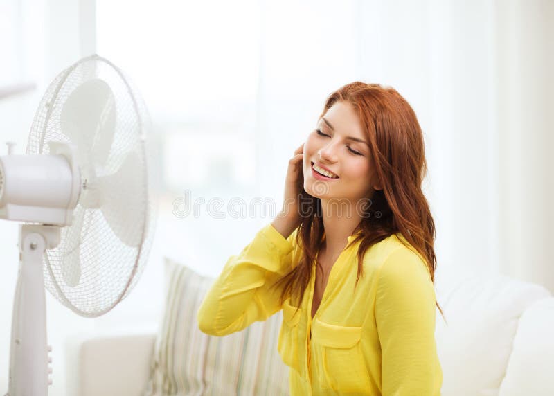 Smiling redhead teenage girl with big fan at home