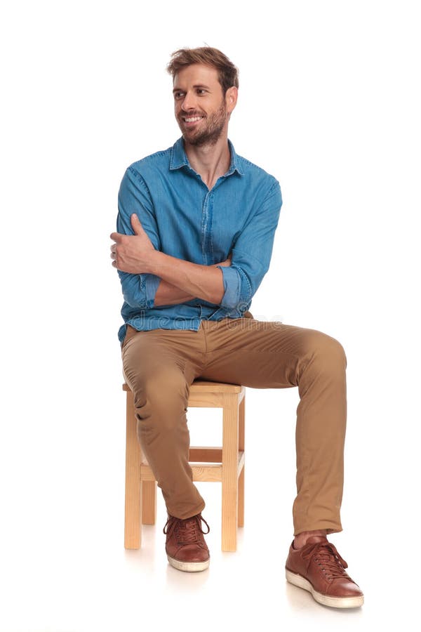 Smiling seated young casual man looks to side on white background